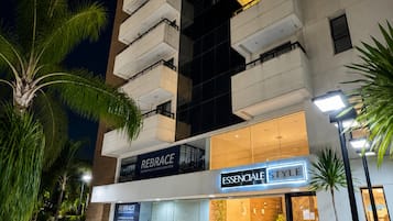 Un hotel moderno con un llamativo letrero 'REBRACE', una entrada bien iluminada y un área exterior ajardinada con palmeras.