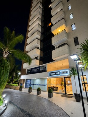 A modern hotel with a prominent 'REBRACE' sign, a well-lit entrance, and a landscaped outdoor area with palm trees.