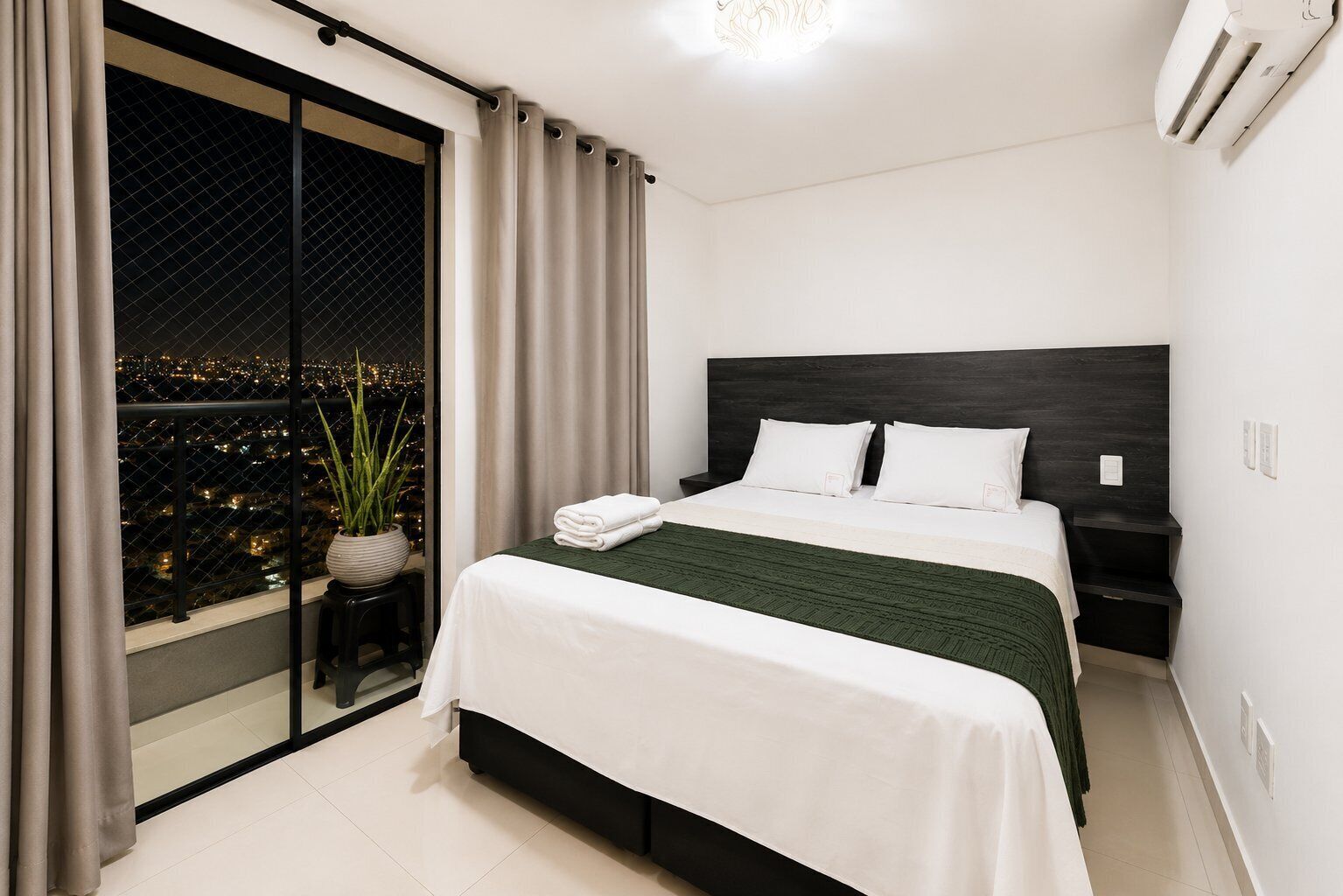 A modern bedroom with a bed, a nightstand, a potted plant, and a view of the city at night.