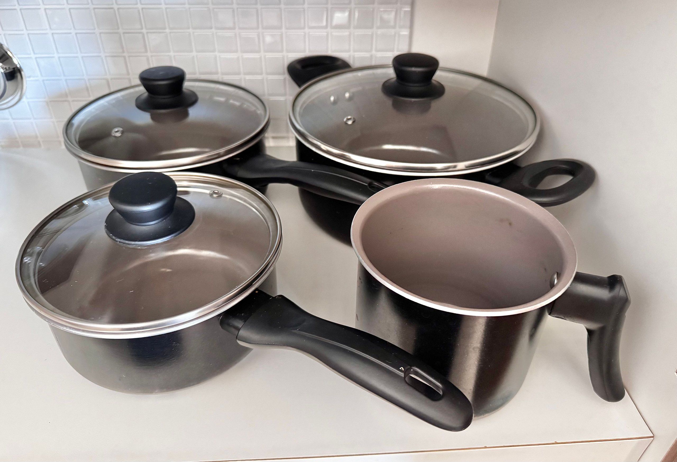 Four stainless steel pots with lids and handles on a kitchen counter.