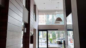 Un hall d’hôtel moderne avec une entrée en verre, des panneaux de bois et un sol épuré et réfléchissant.