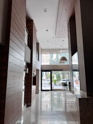 A modern hotel lobby with a glass entrance, wooden paneling, and a clean, reflective floor. - Essencialle Style 1Q (Goiânia)