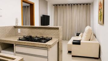 A compact kitchen with a gas stove, a small countertop, and a built-in oven. There is a beige sofa with a cushion and a flat-screen TV mounted on the wall.