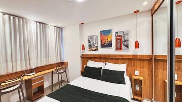 A hotel room with a bed, desk, chair, and a wall with pictures.