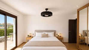 Quarto com uma cama grande, luminária no teto e porta de vidro deslizante para área externa.