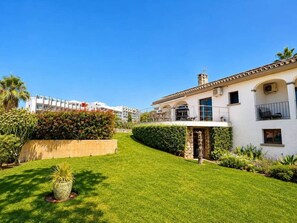 A white building with a stone facade, a well-maintained lawn, and a clear blue sky. - Villa with Private Pool and Mediterranean Gardens (La Capellania)