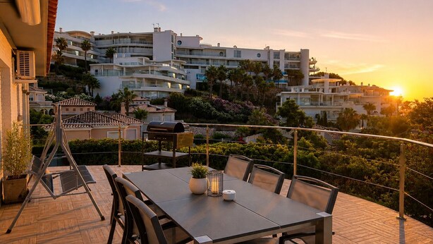 Um terraço com mesa e cadeiras, churrasqueira e vista para uma colina com edifícios.