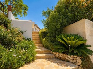A stone pathway leading to a building, surrounded by lush greenery and a stone wall. - Villa with Private Pool and Mediterranean Gardens (La Capellania)