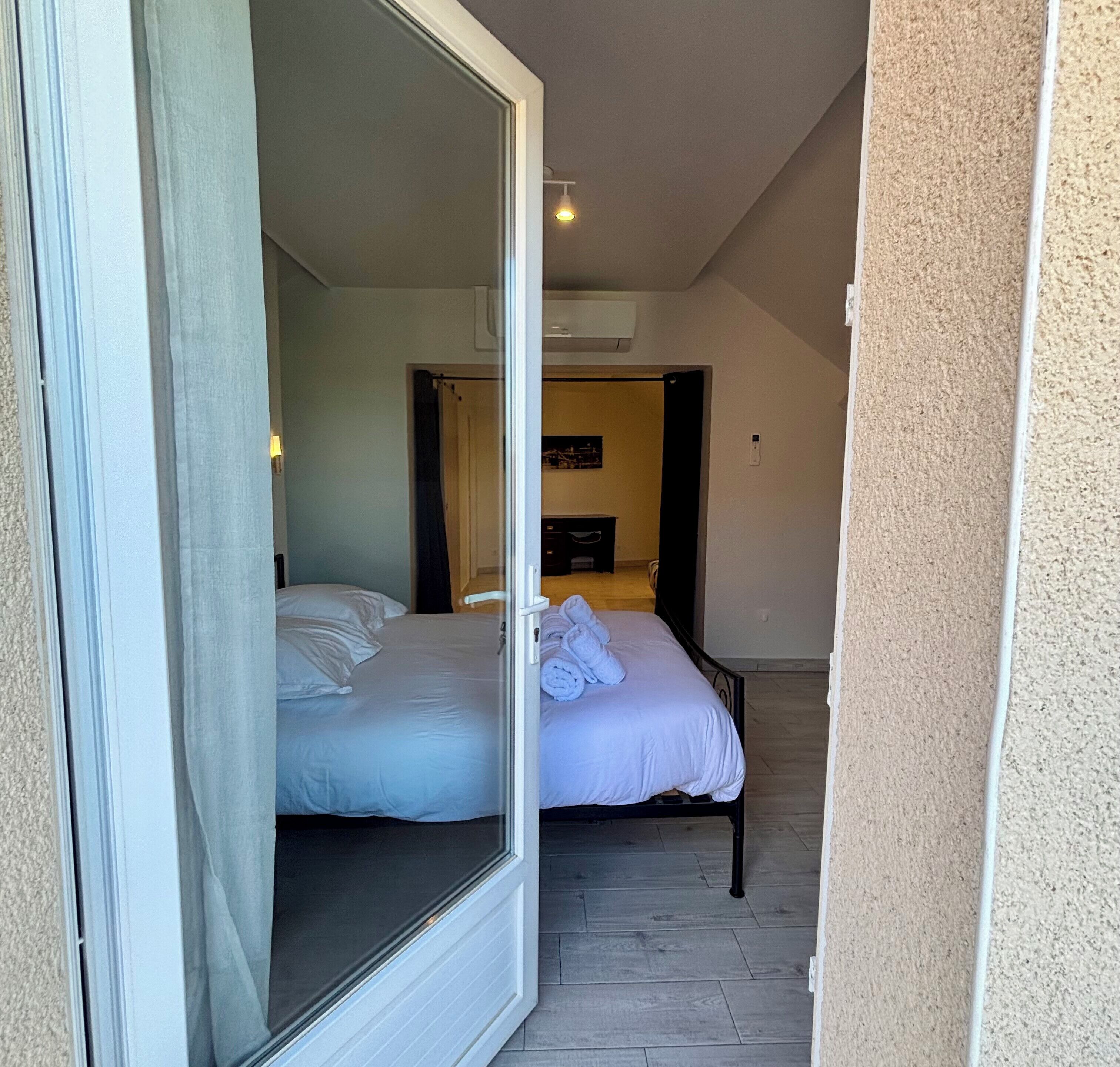 A bedroom with a bed, a window, and a door leading to another room.