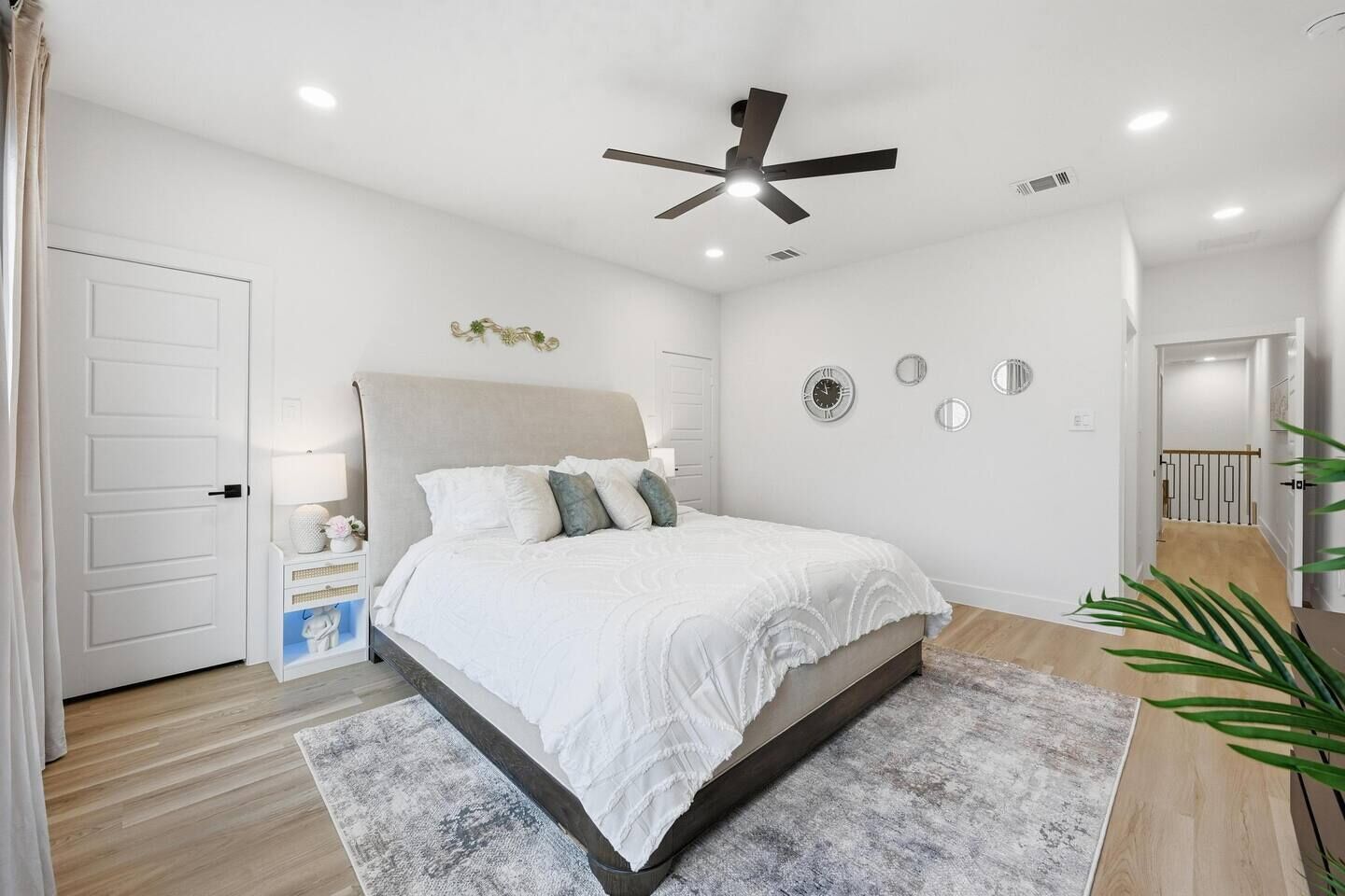 Quarto com cama, ventilador de teto, mesa de cabeceira e relógio de parede.