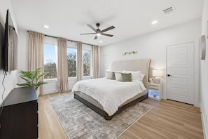 Ein Schlafzimmer mit Bett, Deckenventilator, Fernseher und einer Pflanze.