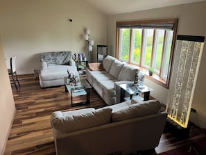 Un salon moderne avec un canapé, une table basse et une table d’appoint. Une fenêtre offre une vue sur la verdure à l’extérieur.