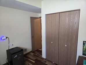 A room with a wooden wardrobe, a desk with a computer, and a wall-mounted TV.