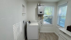 A laundry room with a washing machine, a water heater, and a window with blinds. - Fully Renovated 4-Bedroom, 3-Bath Home in the Heart of Austin's Attractions (Austin)