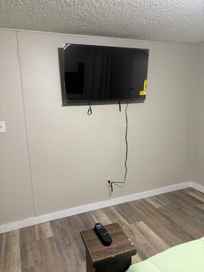 Habitación con televisión montada, una mesita de madera con un control remoto y suelo de madera.