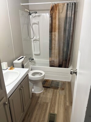Casa de banho com sanita, lavatório, chuveiro e suporte para toalhas.