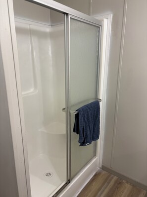A glass-enclosed shower with a towel rack and a drain.