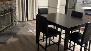 Ein Essbereich mit Kamin aus Stein, einem Tisch mit Stühlen und einer Küche im Hintergrund.