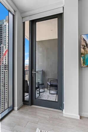Een balkon met een glazen deur, uitzicht op een stadsgezicht en een schilderij aan de muur.