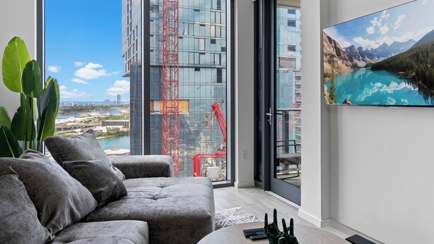 Un salón moderno con un sofá gris, una mesa de centro y un ventanal con vistas a una obra en construcción.