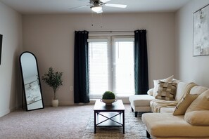 A living room with a ceiling fan, a sofa, a coffee table, a potted plant, and a large mirror.