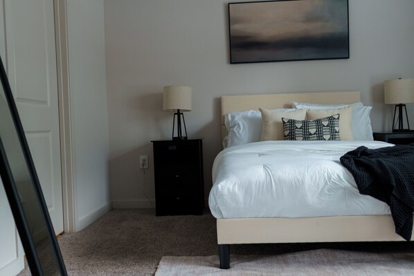 A bedroom with a bed, two bedside tables, a lamp, and a wall-mounted painting.