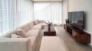 Una sala de estar moderna con un sofá modular, una mesa de centro, un televisor sobre un mueble de madera y una lámpara colgante.
