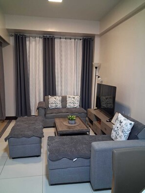 A modern living room with a grey sofa set, a coffee table with a plant, a TV, and a lamp. - Mactan Infinity Pool View|Near Airport & Beach (Lapu-Lapu)