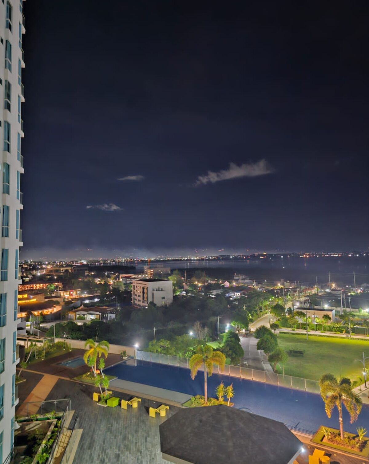 Vista nocturna de un paisaje urbano con una masa de agua, edificios y una zona de piscina.