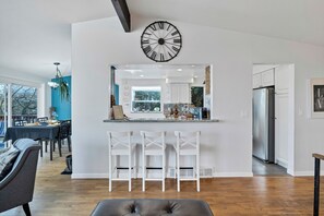 Eine moderne Küche mit einer großen Uhr, weißen Barhocker und einem Essbereich mit Tisch und Stühlen.