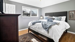 A bedroom with a bed, a nightstand, a lamp, a window, and a door. - Seattle Skyline & Lake Retreat | 3Bd/3Ba (Seattle)