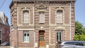 Un edificio histórico de ladrillo con una entrada central, ventanas grandes con contraventanas y un letrero que indica 'RUE CAMP DE GREUEN'.