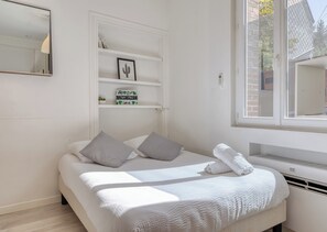 A neatly arranged bedroom with a bed, pillows, a shelf with decorative items, a window, and a wall-mounted mirror. - Shelter 2 - joli studio proche gare (Rouen)