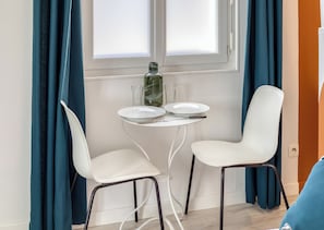 Un petit coin repas avec une table blanche, deux chaises blanches, une bouteille en verre et une assiette.