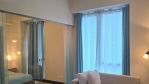 A modern hotel room with a bed, a sofa, a coffee table, and a desk. - Mactan Newtown Poolside View near Airport & Beach (Lapu-Lapu)