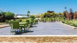 An outdoor patio with green chairs and tables, surrounded by plants and a clear blue sky. - Mactan Newtown Poolside View near Airport & Beach (Lapu-Lapu)