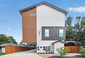 Ein modernes, zweistöckiges Haus mit einer Mischung aus Holz- und weißer Fassade, einer sichtbaren Garage und einem Vorgarten mit Bepflanzung.
