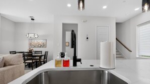 A modern kitchen with a stainless steel sink, a dining area with a table and chairs, and a staircase leading to another level. - 2BR Retreat | 5 Min Downtown + Medical District (Dallas)