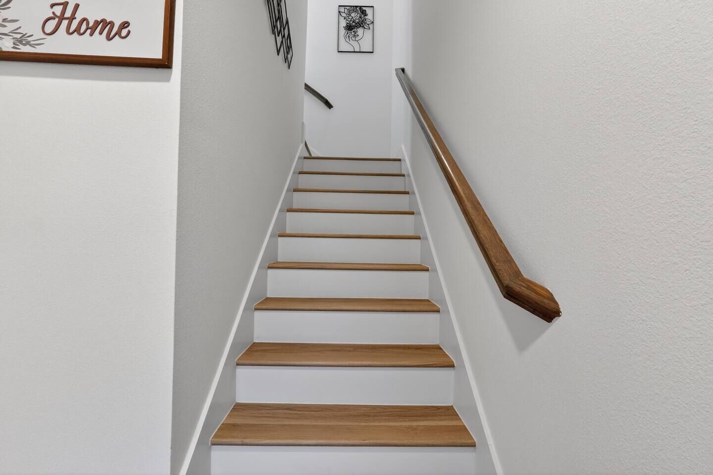 A staircase with wooden steps and a wooden handrail, white walls, and a framed word 'Home' on the left.