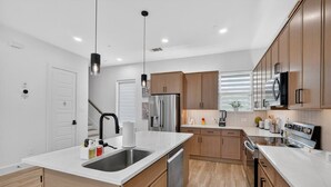 A modern kitchen with a central island, stainless steel appliances, and wooden cabinetry. - 2BR Retreat | 5 Min Downtown + Medical District (Dallas)