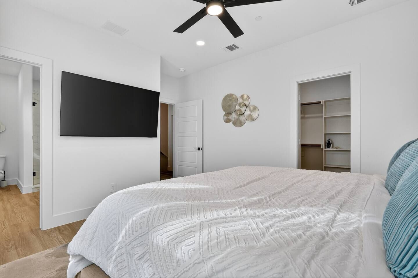 A bedroom with a bed, a ceiling fan, a TV, and built-in shelving.