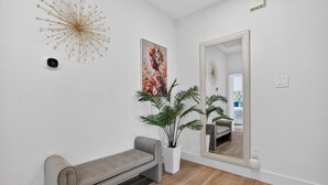 A modern interior with a bench, a large mirror, a wall-mounted light fixture, and a potted plant. - 2BR Retreat | 5 Min Downtown + Medical District (Dallas)