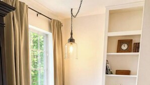 A bedroom with a bed, a window, a bookshelf, and a hanging light fixture. - Shady Pecan Farmside (Red Oak)