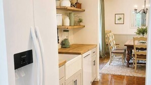 A modern kitchen with white cabinetry, a built-in refrigerator, a wooden countertop, and a dining area with a table and chairs. - Shady Pecan Farmside (Red Oak)
