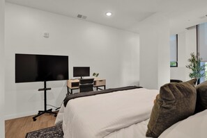 A modern hotel room with a large bed, a desk with a computer, and a flat-screen TV. - Cozy Modern 1BR in Downtown OTR, GYM, POOL (Cincinnati)