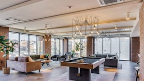 Een ruime woonkamer met een pooltafel, comfortabele zithoeken, grote ramen en uitzicht over de stad.
