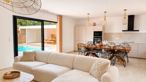 Eine moderne Küche mit Essbereich, einer Couch und Blick auf einen Außenpool.