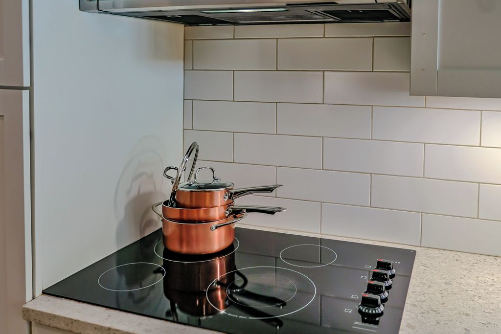 A kitchen with a black induction cooktop, a copper pot, and a white tiled backsplash.