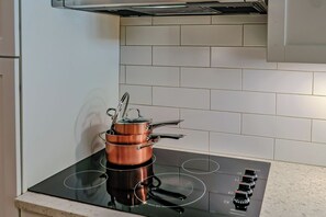 A kitchen with a black induction cooktop, a copper pot, and a white tiled backsplash. - The New Amsterdam Nook: European-inspired guest suite in Mechanicsville. Features 2 bedrooms, 1 spa-like bath, full kitchen, indoor fireplace, dedicated workspace. Enjoy a large yard with pool, hot tub, playground, and BBQ. Comfortably fits 4-6. (Mechanicsville)