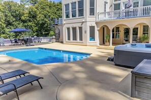 Une piscine avec des chaises longues, un jacuzzi et un patio couvert.